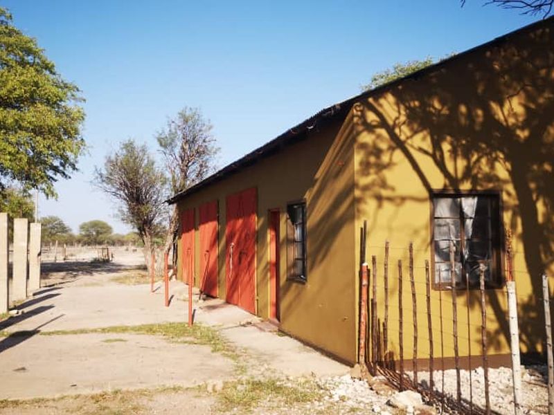 Rear view of a farm outbuilding featuring multiple garage bays, concrete apron, and wire fencing on a rural property.