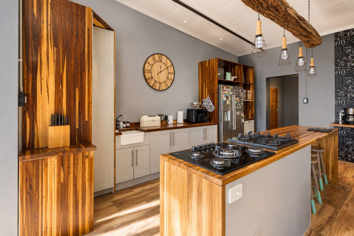Modern farmhouse kitchen featuring wooden countertops, a butler sink, a central island with a gas hob, and rustic exposed timber beam ceiling accents.