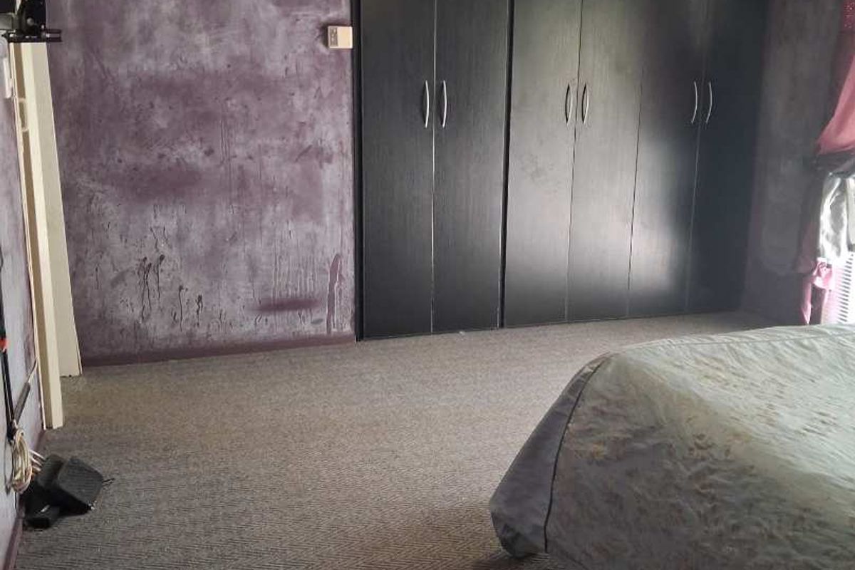 A bedroom featuring built-in dark cabinetry, carpeted flooring, and a ceiling fan, requiring cosmetic updates to the wall finishes.