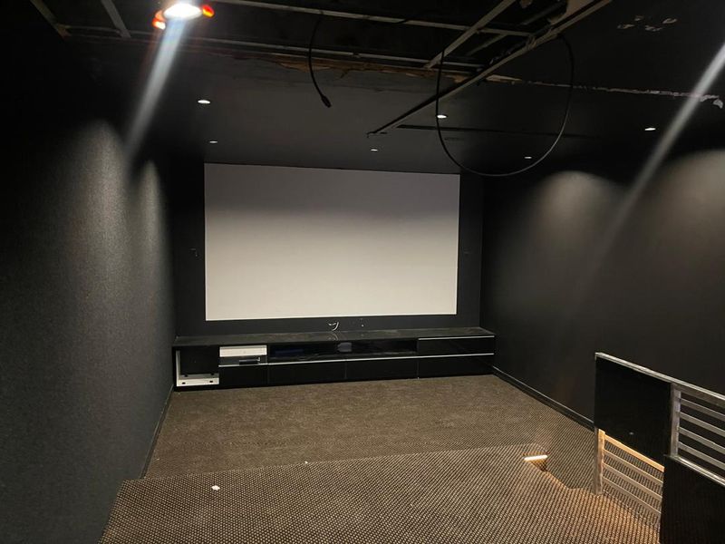 A dedicated cinema room featuring a projector screen, built-in media cabinetry, and tiered flooring, currently requiring ceiling completion and electrical finishing.
