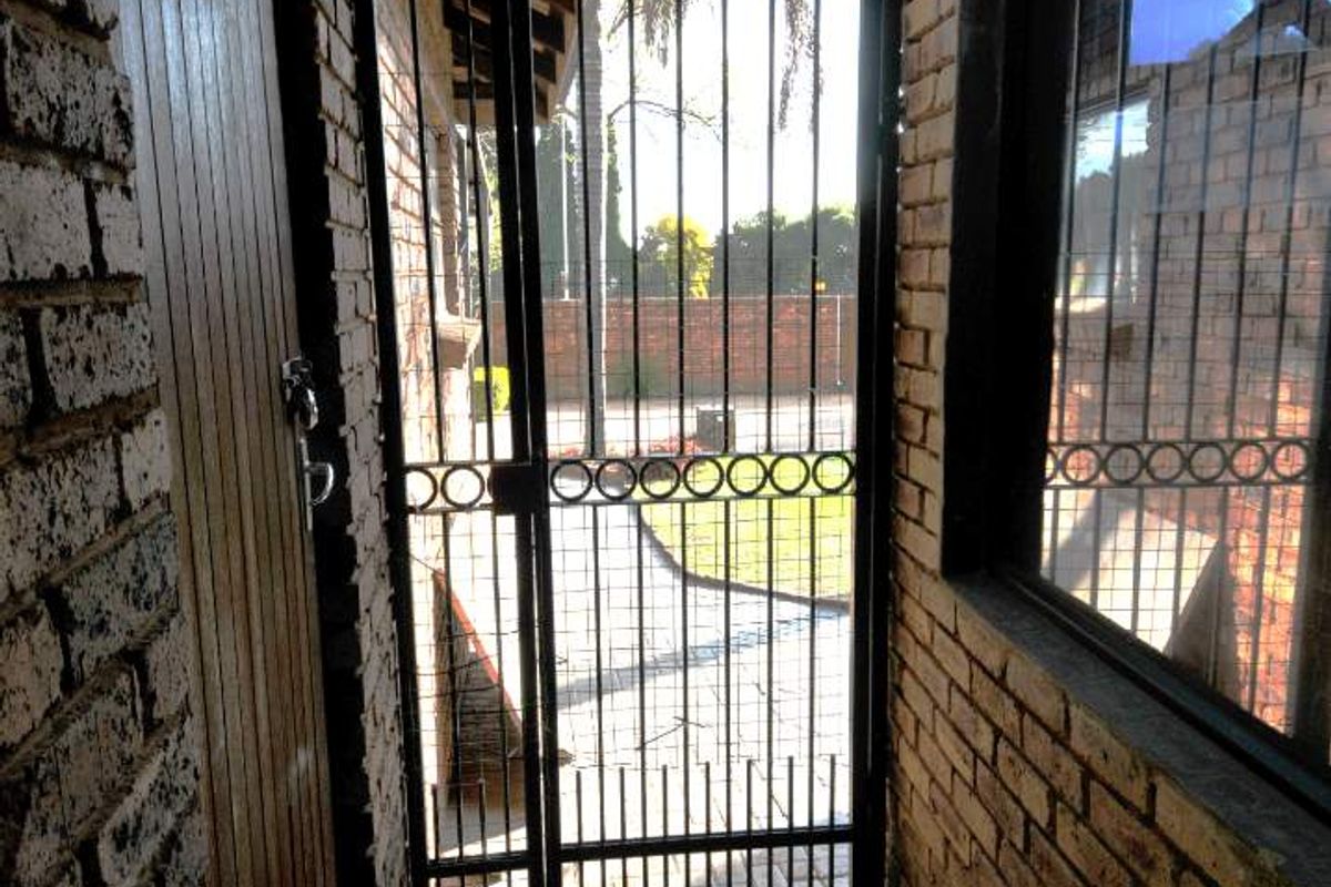 A narrow exterior walkway featuring exposed brick walls, brick paving, and a secure metal gate leading to the rear garden area.