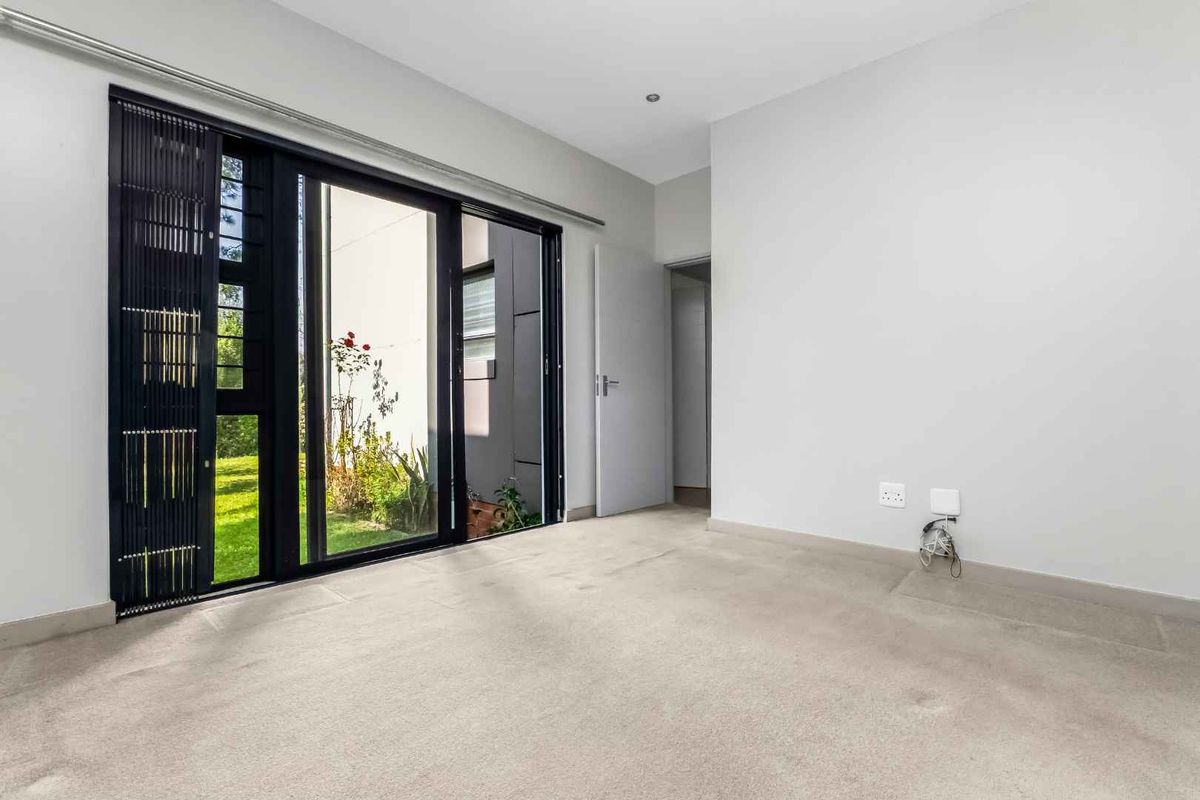 A bright, empty bedroom featuring neutral carpeting, clean walls, and large sliding glass doors providing direct access to an outdoor garden area.