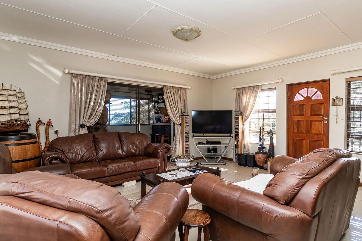Spacious living room featuring tiled flooring, coved cornicing, and direct access to the exterior via a sliding glass door and timber entrance door.