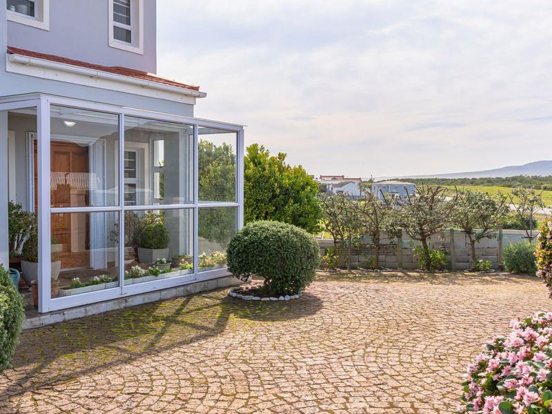 A well-maintained rear exterior featuring a glass-enclosed patio, paved courtyard area, and established garden with scenic landscape views.