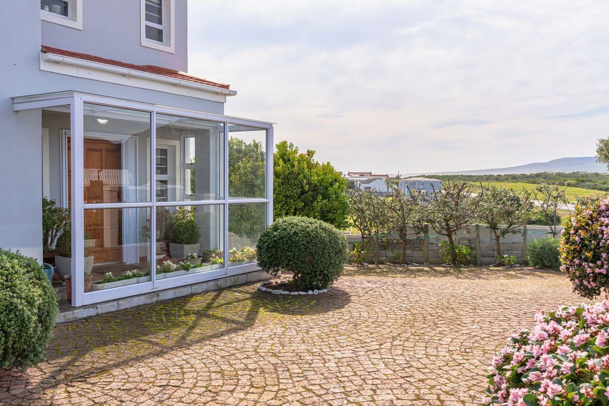 A well-maintained rear exterior featuring a glass-enclosed patio, paved courtyard area, and established garden with scenic landscape views.