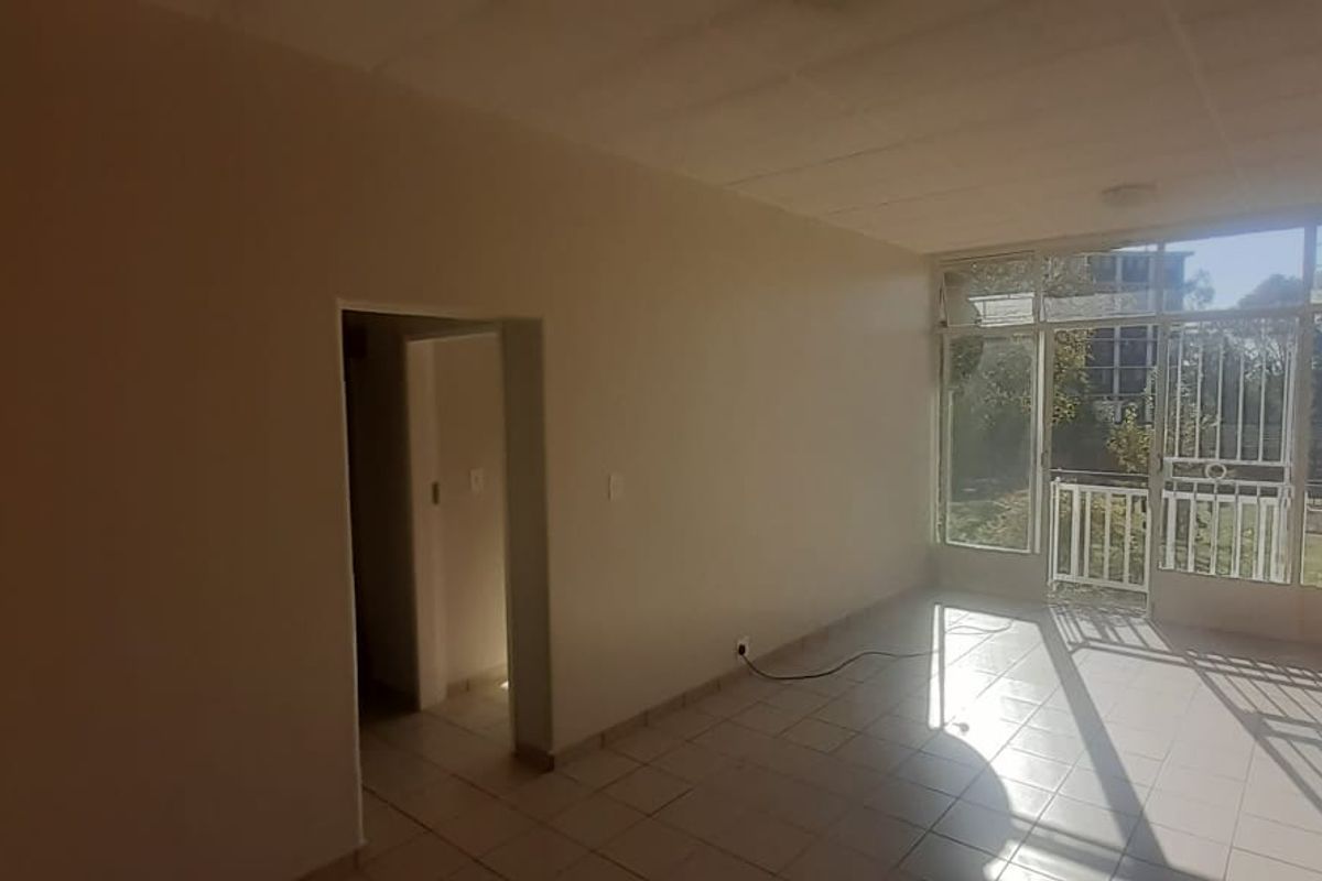 An empty living area featuring tiled flooring, a decorative exposed brick feature wall, and large windows providing natural light and garden access.