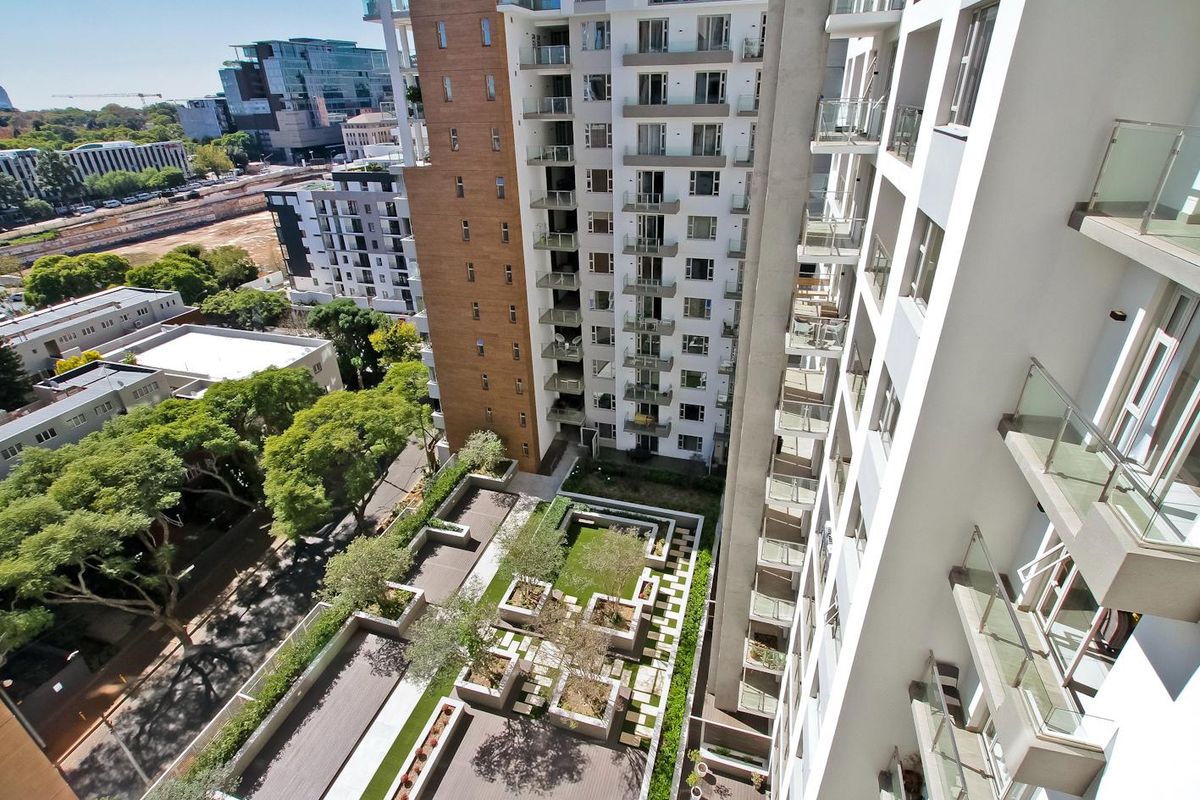High-angle aerial view of the apartment complex, showcasing the building facade, private balconies, and the landscaped courtyard area below.