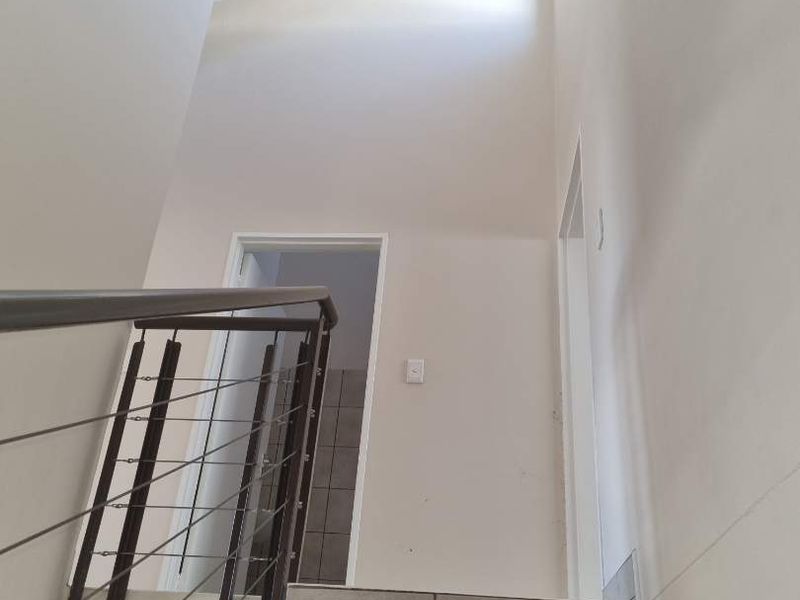 A bright, modern staircase featuring tiled steps and a sleek metal balustrade, leading to an upper level with high ceilings.
