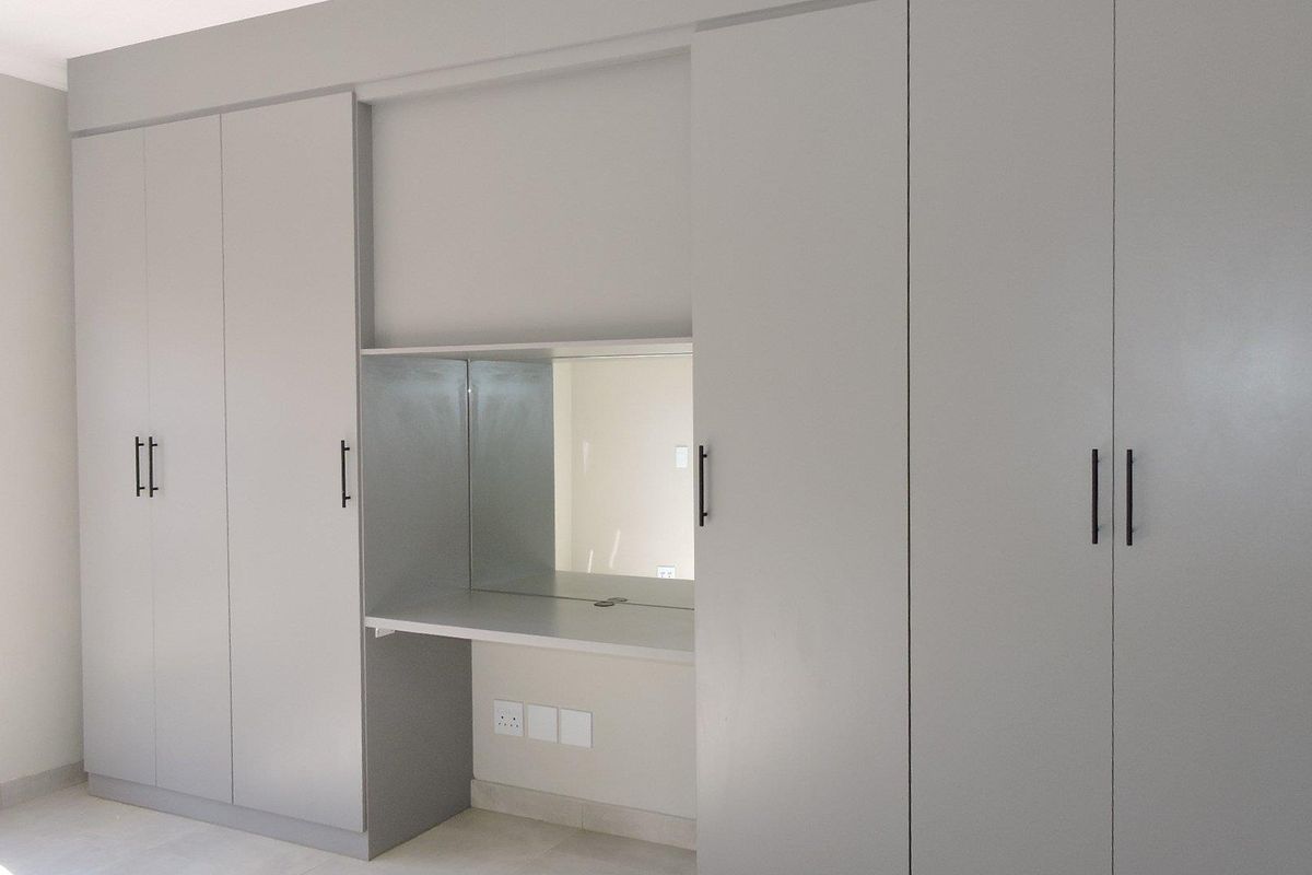 A bright bedroom featuring modern, floor-to-ceiling built-in cupboards with an integrated vanity desk and mirror.