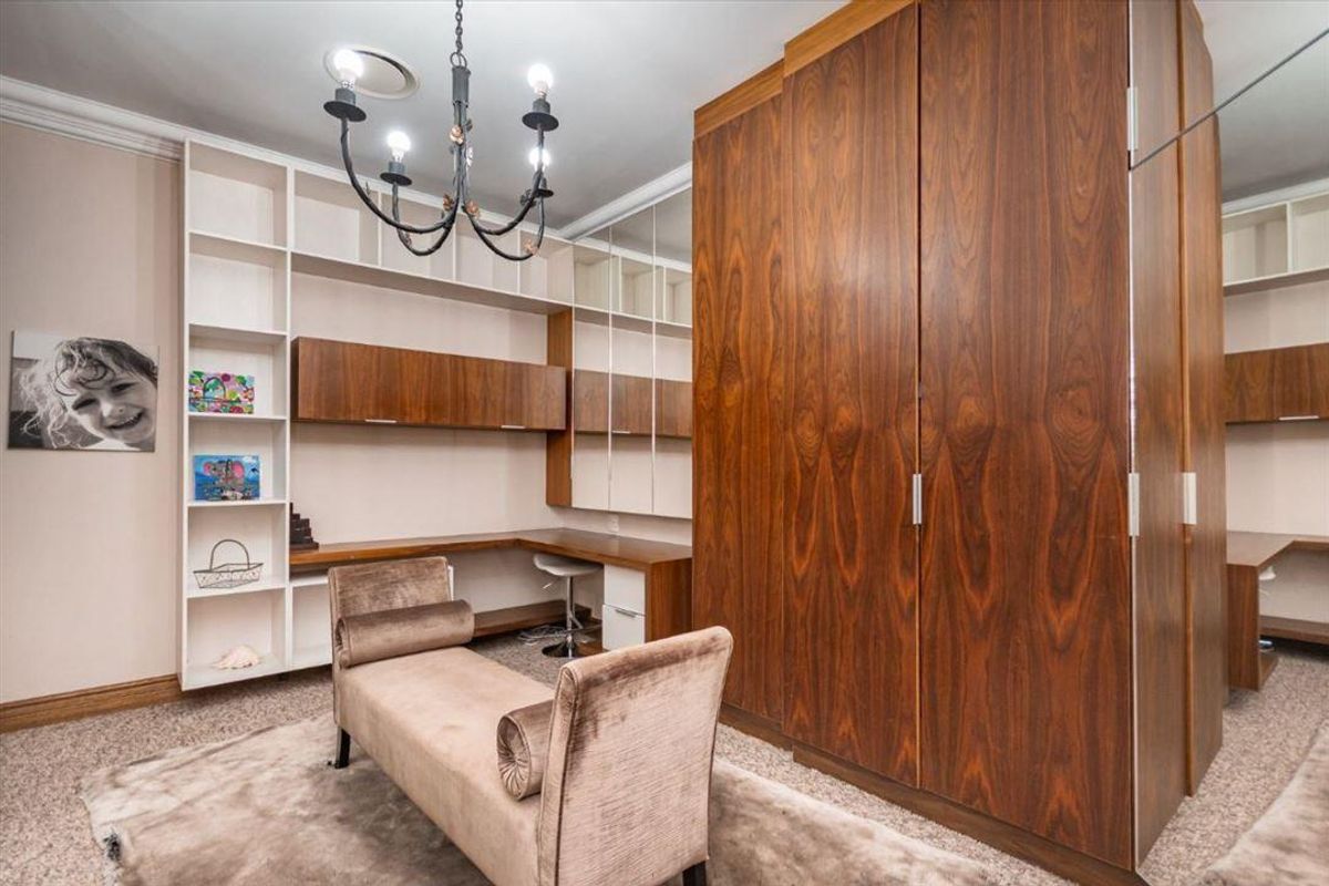 A well-appointed bedroom featuring extensive built-in wooden cabinetry, integrated desk space, and mirrored wardrobe doors, providing ample storage and functional workspace.