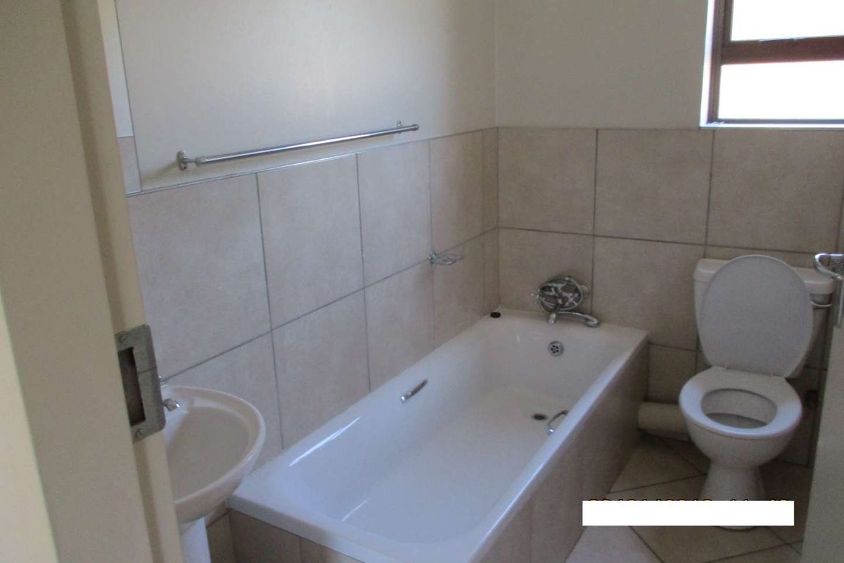 A functional bathroom featuring a pedestal basin, built-in bathtub, and toilet with neutral wall and floor tiling.