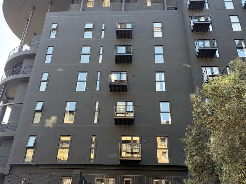 A modern multi-story apartment building facade featuring dark exterior finishes, multiple private balconies with metal railings, and uniform casement windows.