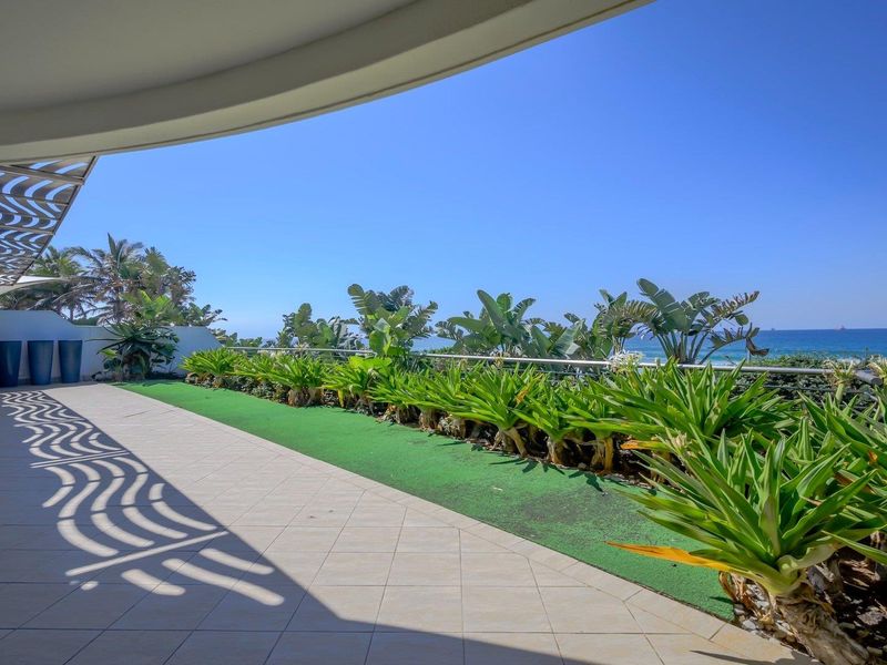 Spacious covered balcony featuring tiled flooring, a stainless steel balustrade, and an artificial grass border, offering expansive ocean views.
