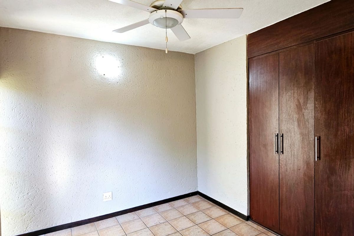 A vacant bedroom featuring tiled flooring, a ceiling fan, and a large built-in wooden wardrobe with modern handles.