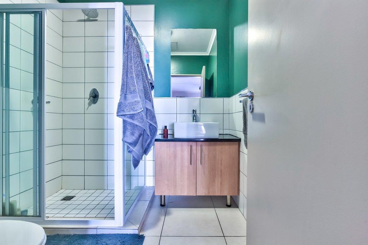 A functional bathroom featuring a glass-enclosed shower, a modern vessel sink vanity with storage, and tiled flooring.