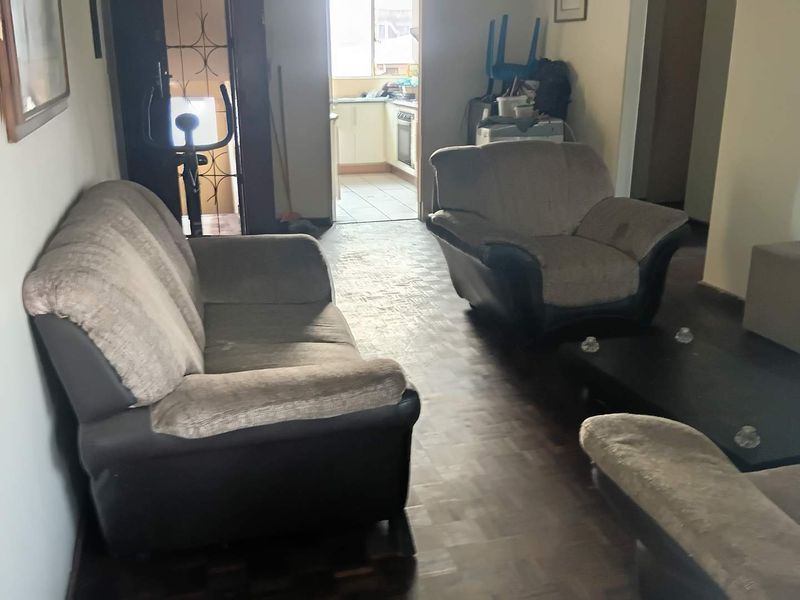Living room area featuring parquet flooring with an open transition to the kitchen space, showing signs of wear and dated finishes.