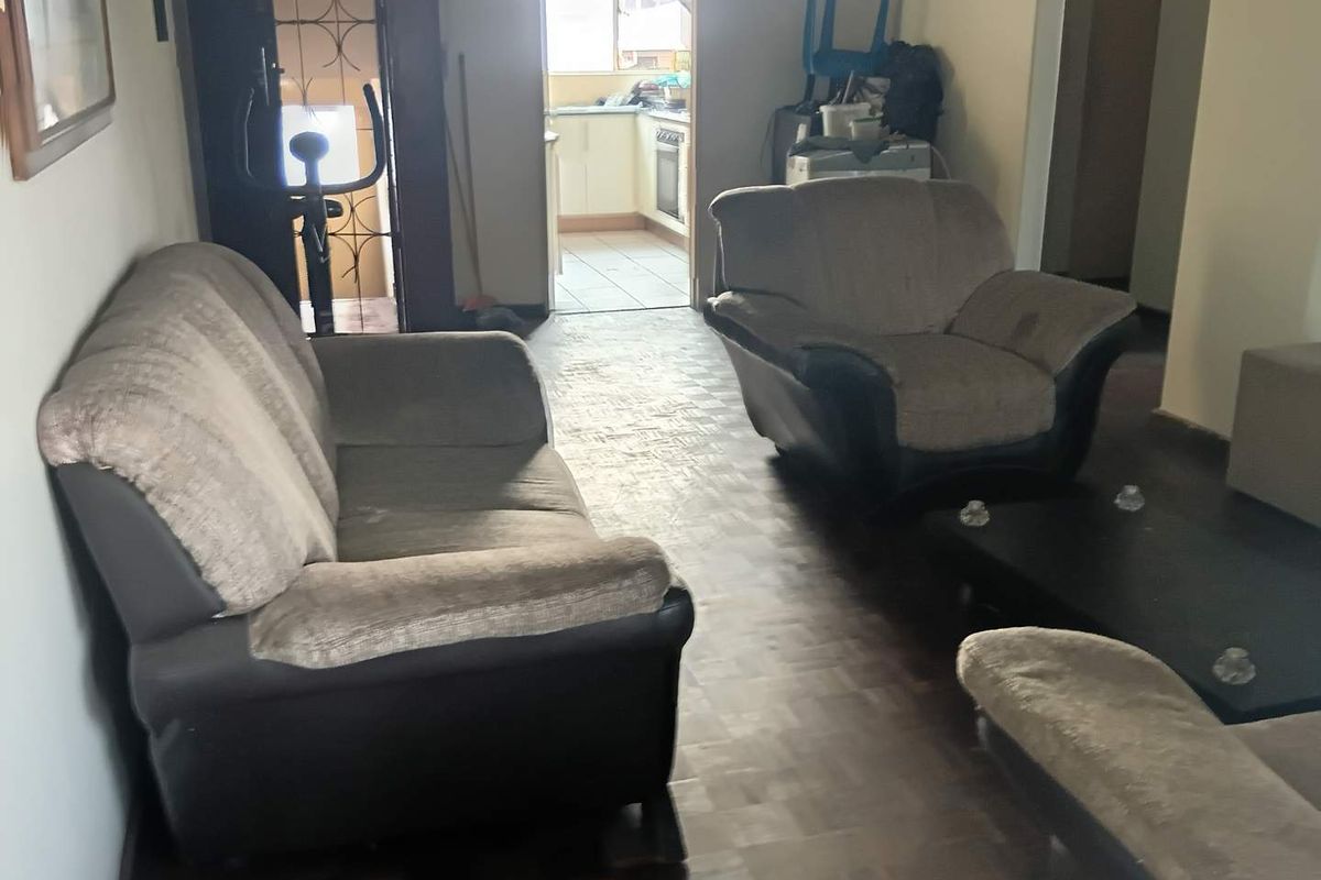 Living room area featuring parquet flooring with an open transition to the kitchen space, showing signs of wear and dated finishes.