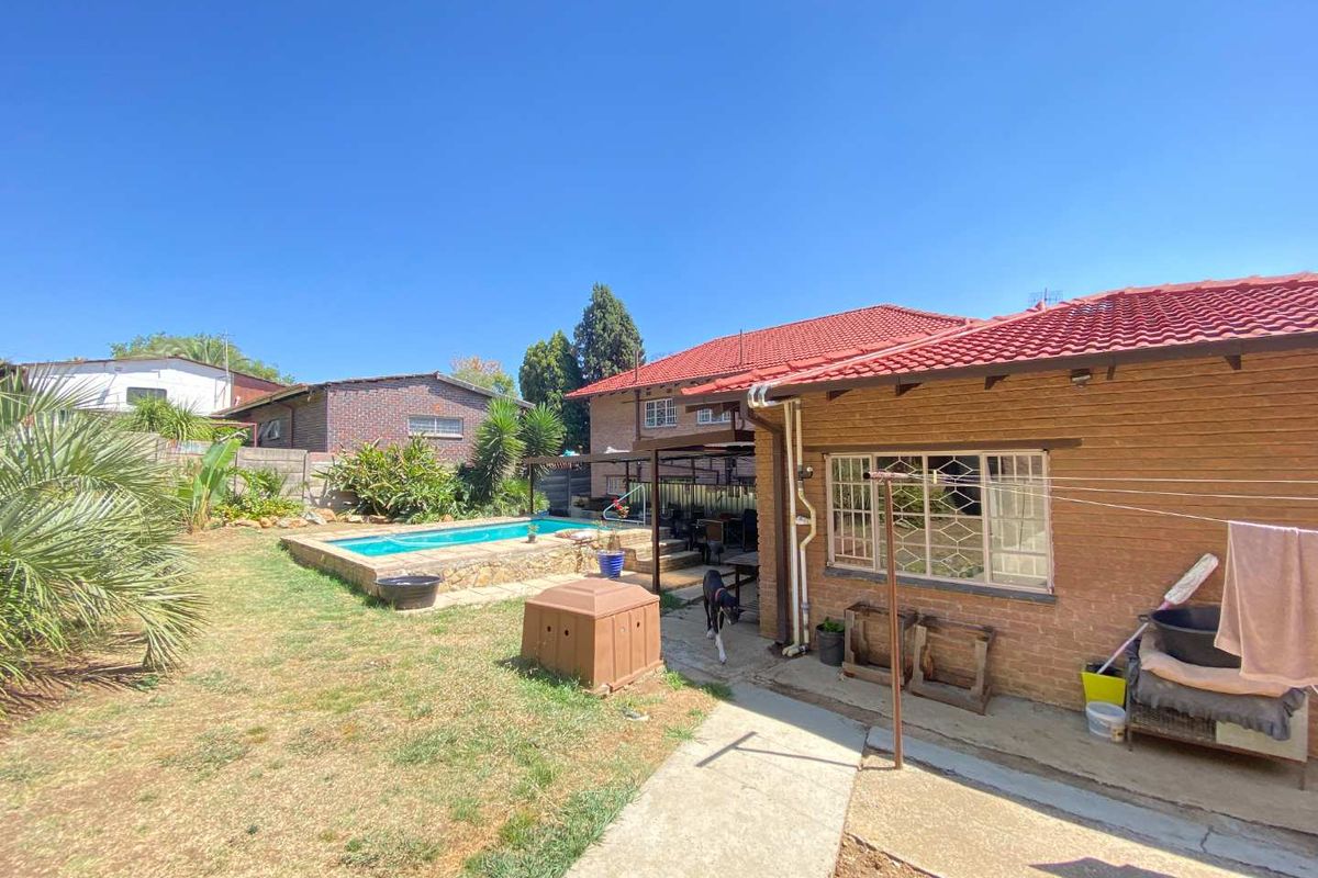 Rear view of the property featuring a swimming pool, paved patio area, and established garden space with brick exterior walls.