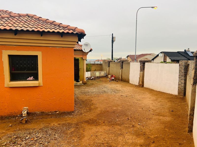 Rear exterior view of the property featuring a tiled roof, perimeter walling, and an unpaved yard area.