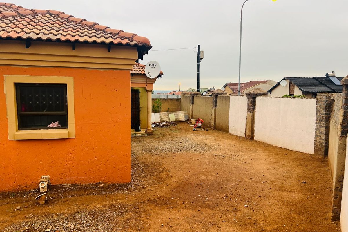 Rear exterior view of the property featuring a tiled roof, perimeter walling, and an unpaved yard area.