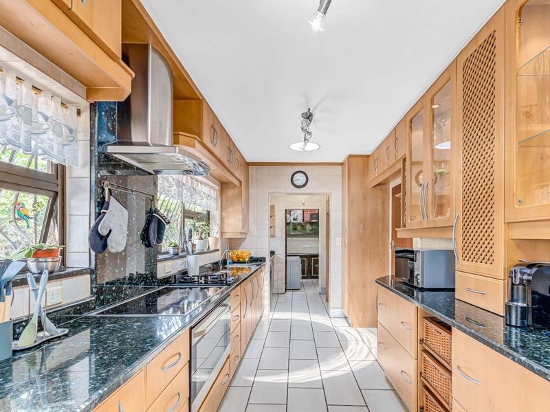 A functional galley-style kitchen featuring light wood cabinetry, dark granite countertops, tiled flooring, and integrated stainless steel appliances.