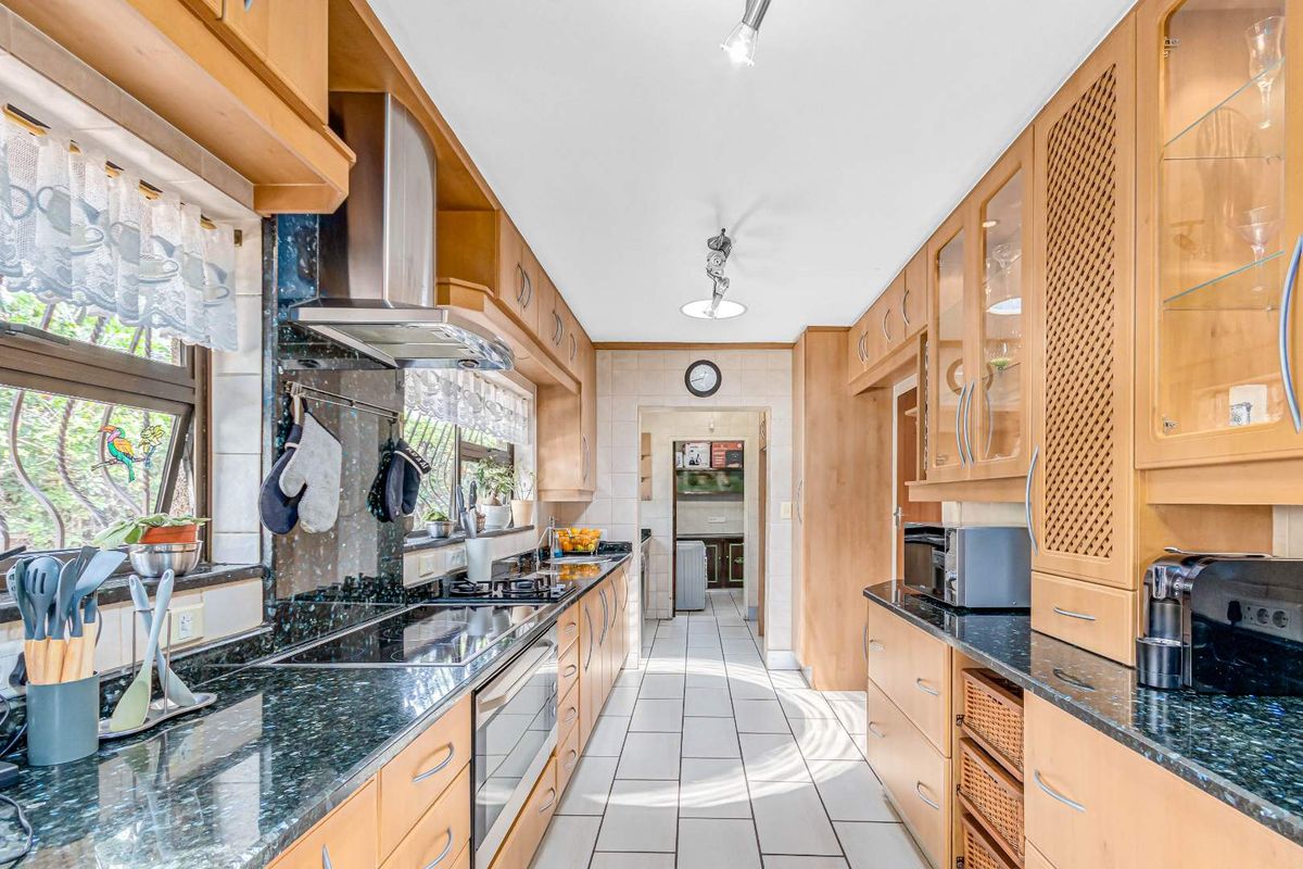 A functional galley-style kitchen featuring light wood cabinetry, dark granite countertops, tiled flooring, and integrated stainless steel appliances.