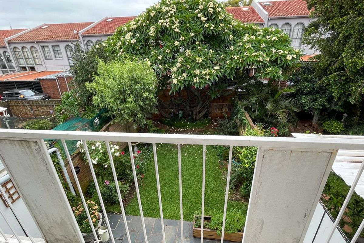 Elevated view from a balcony overlooking a private rear garden with mature landscaping, slate paving, and a metal safety balustrade.