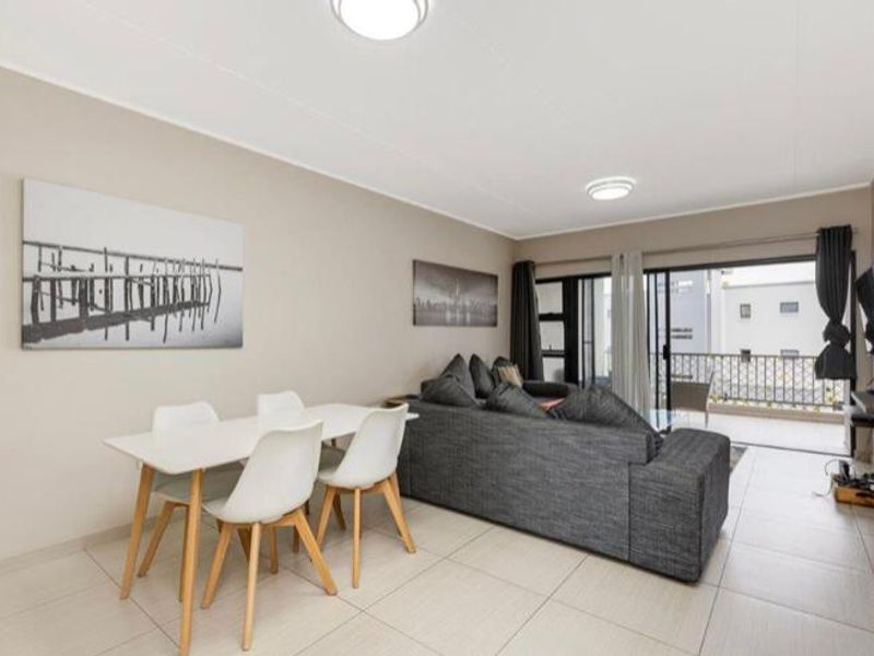 An open-plan living and dining area featuring neutral tiled flooring and direct access to a balcony through sliding glass doors.