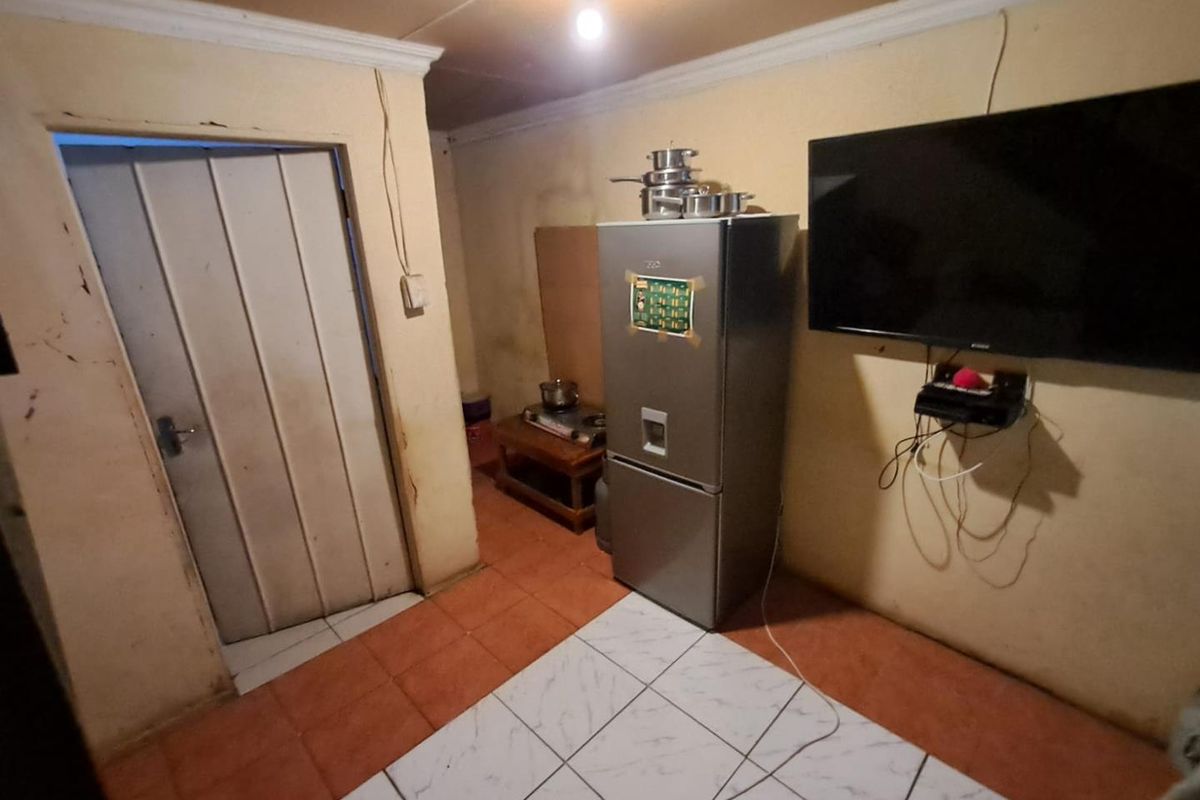 A small, basic living area featuring mixed floor tiling, plain walls, and a simple door, requiring cosmetic updates and maintenance.