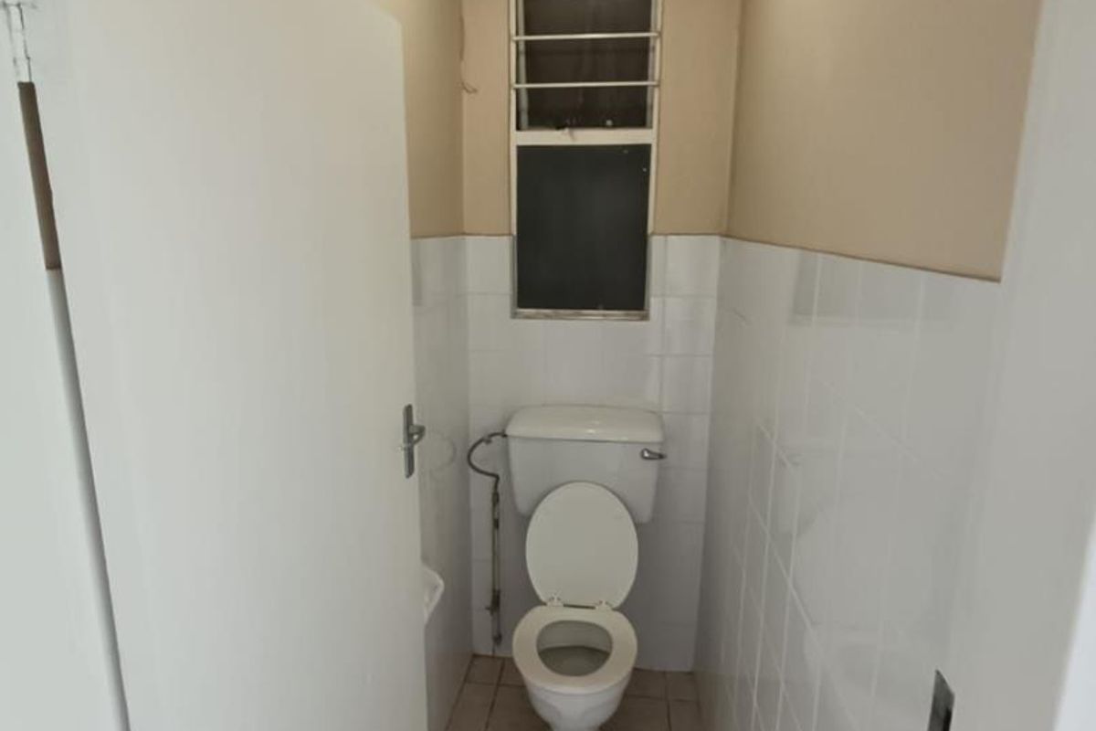 A compact, functional bathroom featuring tiled walls, tiled flooring, and a window with security bars.