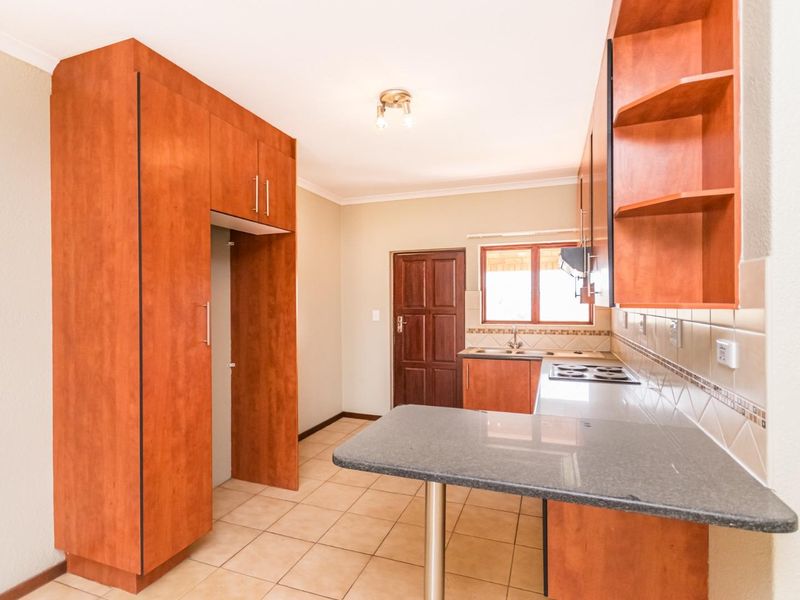 A functional kitchen featuring wood-finish cabinetry, granite-look countertops, a built-in hob, and tiled flooring, offering a clean and practical workspace.