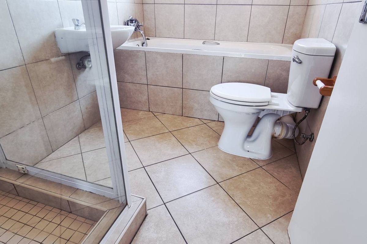 A functional bathroom featuring a separate shower enclosure, a built-in bathtub, a pedestal basin, and a standard toilet with tiled walls and flooring.