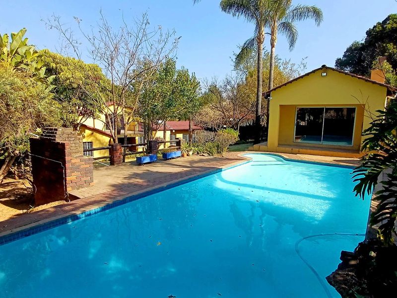Outdoor pool area featuring a swimming pool, paved patio, and a brick built-in braai, set within a mature garden environment.