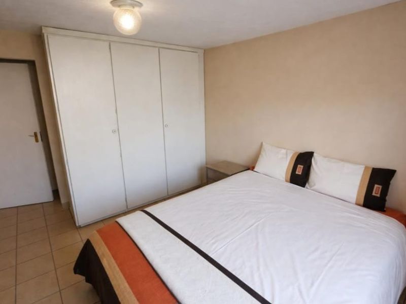 A functional bedroom featuring built-in wardrobes, neutral wall finishes, and tiled flooring.