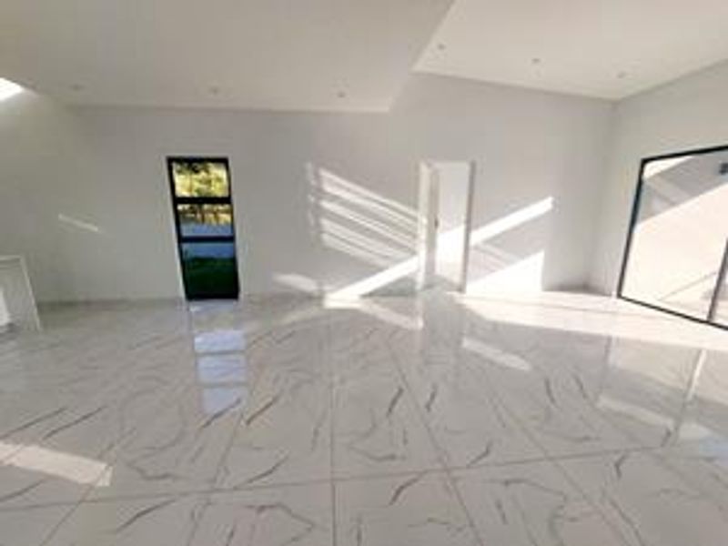 A bright, spacious open-plan living area featuring modern marble-look porcelain floor tiles, recessed lighting, and large aluminium-framed windows and sliding doors.
