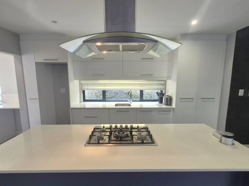 Modern kitchen featuring a central island with a gas hob, sleek white cabinetry, quartz countertops, and a contemporary extractor fan.