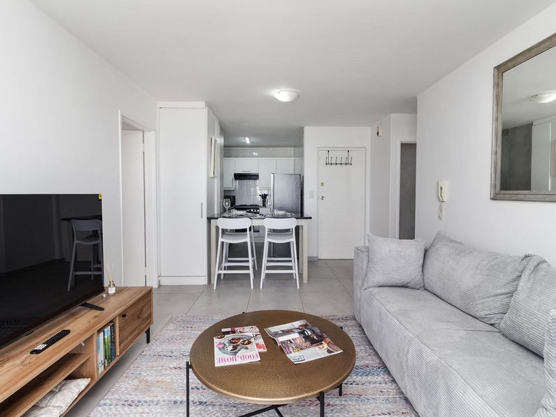 Open-plan living area featuring tiled flooring and a compact kitchen with built-in cabinetry and an extractor fan.
