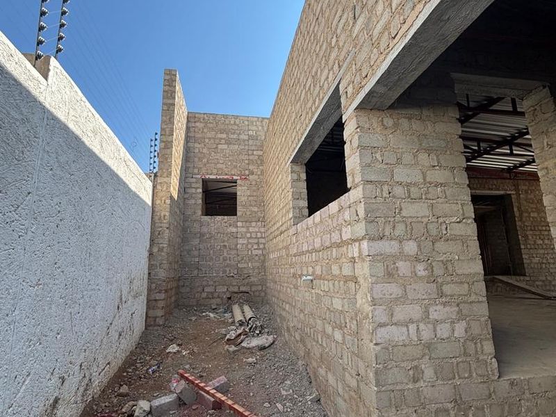 An exterior view of a property under construction, featuring exposed brick walls, concrete lintels, and perimeter electric fencing.
