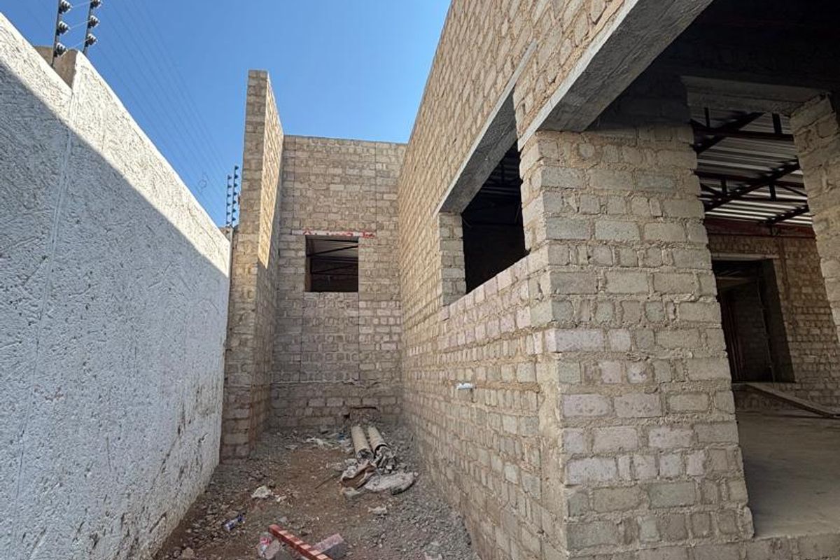 An exterior view of a property under construction, featuring exposed brick walls, concrete lintels, and perimeter electric fencing.