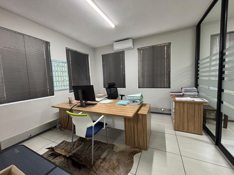 A well-maintained office space featuring tiled flooring, modern glass partitioning, venetian blinds, and a wall-mounted air conditioning unit.