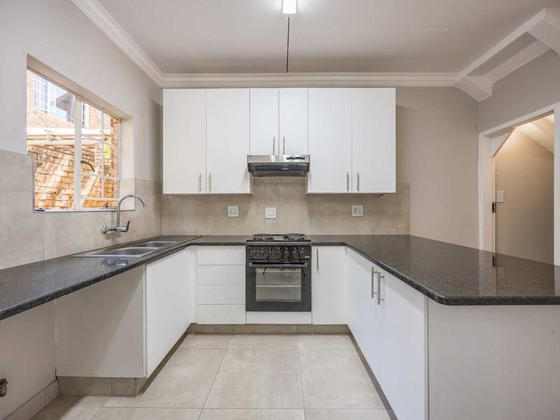 A clean, modern kitchen featuring white cabinetry, dark granite countertops, a built-in oven with extractor fan, and neutral tiled flooring.