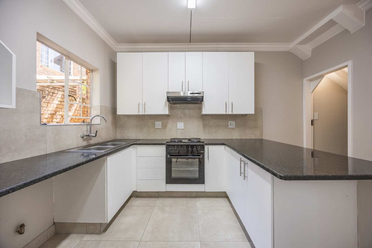 A clean, modern kitchen featuring white cabinetry, dark granite countertops, a built-in oven with extractor fan, and neutral tiled flooring.