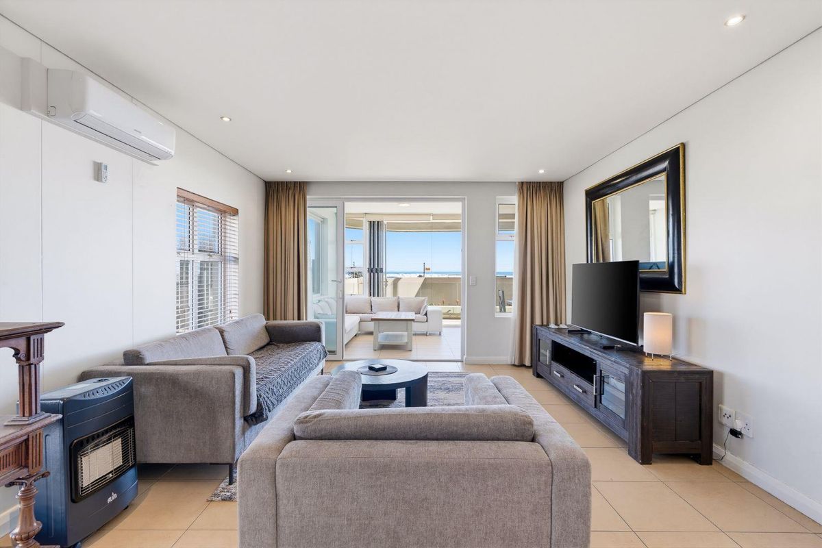 A bright and well-maintained living room featuring tiled flooring, recessed lighting, a wall-mounted air conditioner, and direct access to a balcony with ocean views.