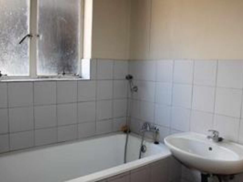 A functional bathroom featuring a standard bathtub, wall-mounted basin, and tiled walls, currently in need of cosmetic updates and maintenance.