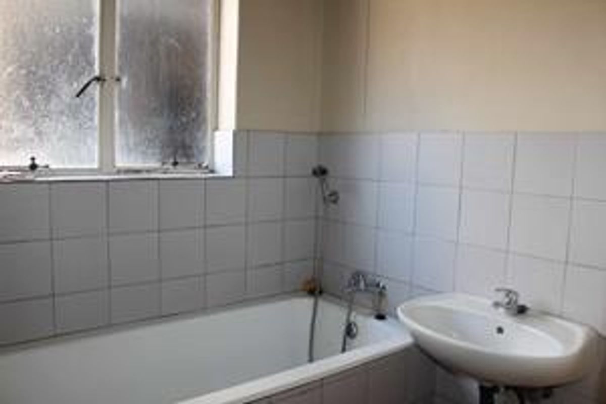 A functional bathroom featuring a standard bathtub, wall-mounted basin, and tiled walls, currently in need of cosmetic updates and maintenance.