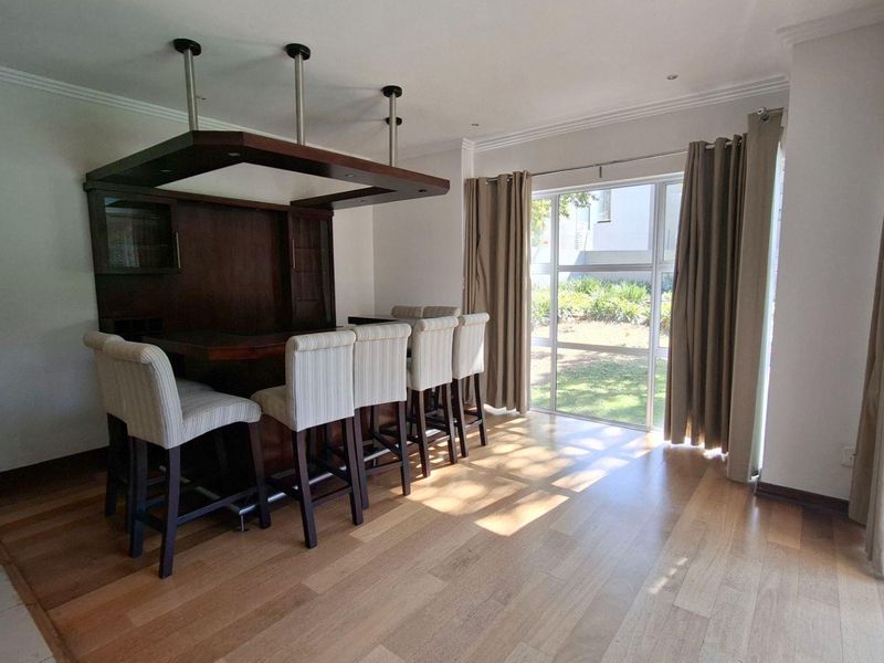 A dedicated bar area featuring a built-in timber counter with an overhead canopy, wood flooring, and large sliding glass doors leading to the garden.
