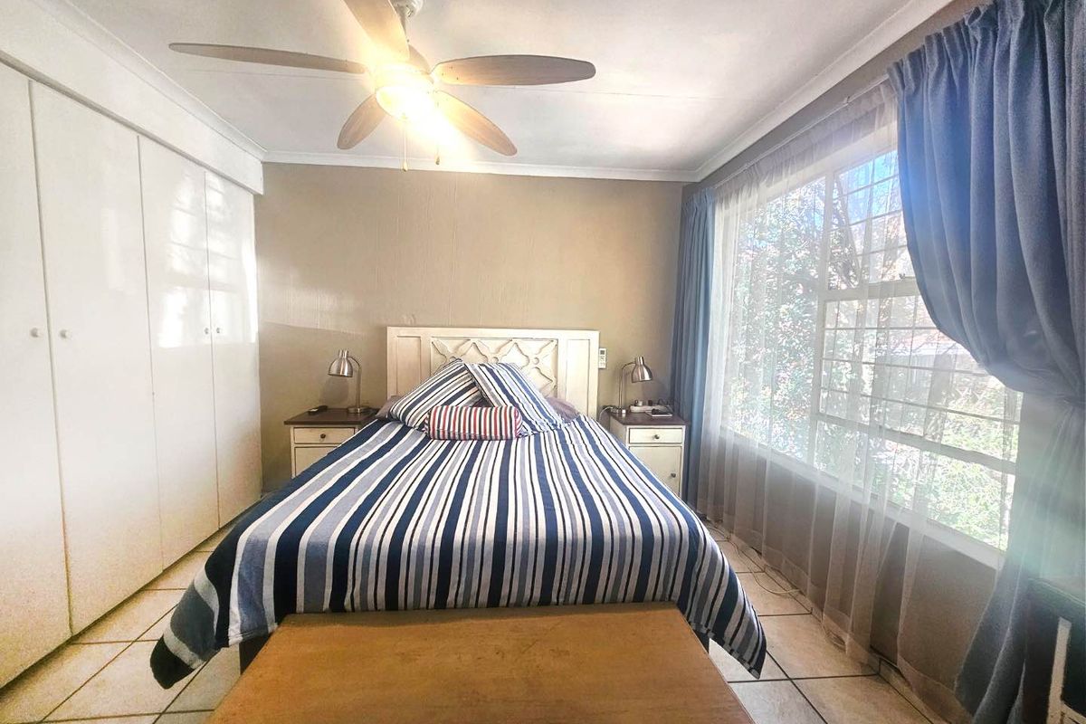 A bedroom featuring built-in cupboards, tiled flooring, and a ceiling fan, with natural light entering through a window fitted with security bars.