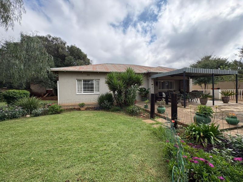 Rear view of the house featuring a lawn, landscaped garden, and a covered patio area with a corrugated metal roof.