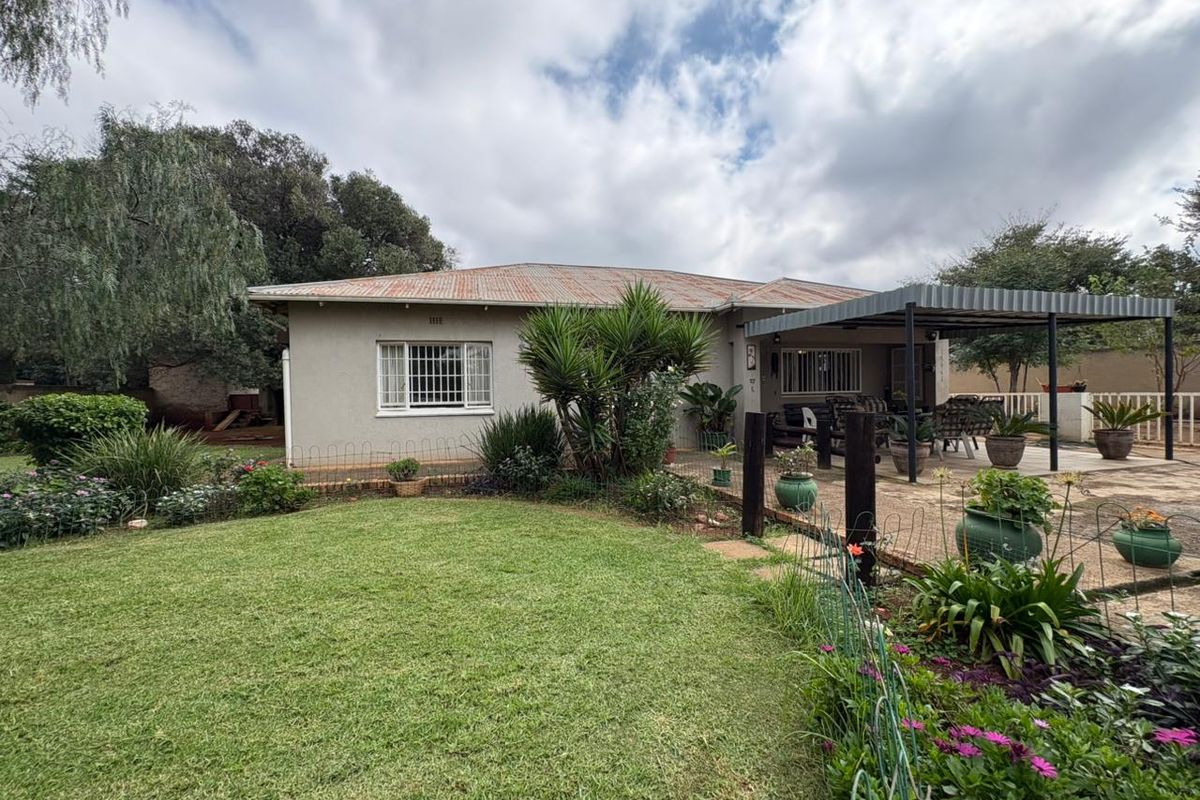 Rear view of the house featuring a lawn, landscaped garden, and a covered patio area with a corrugated metal roof.