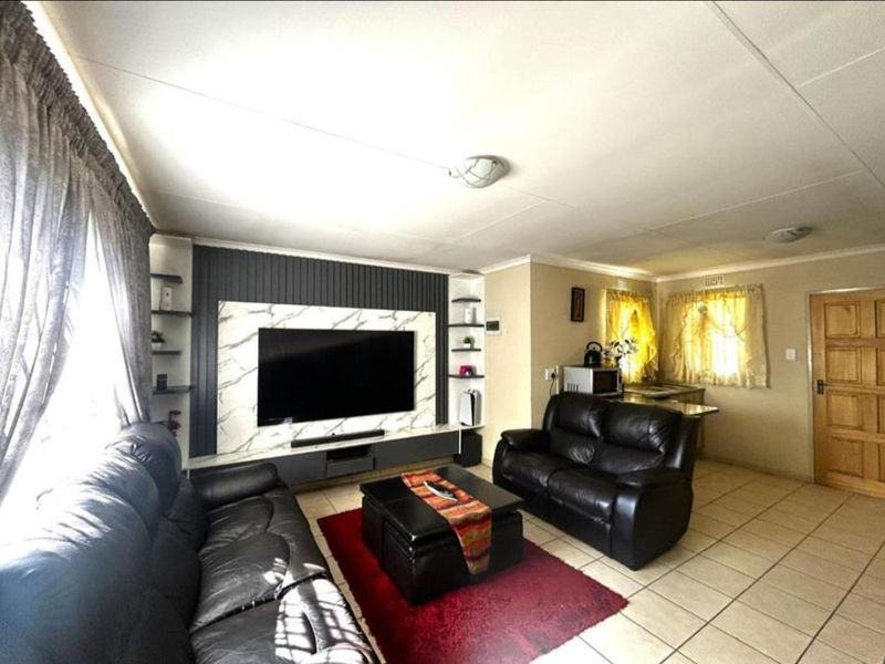 Open plan living area featuring a modern built-in media wall with marble-look paneling and tiled flooring throughout.
